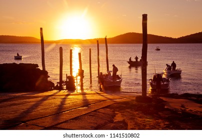 Busy Boat Ramp, Small fishing boats and leisure craft disembark while silhouetted in in front of the setting sun. Queensland, Australia.