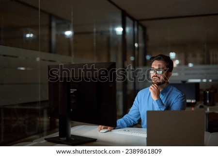 Busy business man software developer using computer working late in office. Professional businessman looking at pc typing searching online solution at night sitting at workplace desk in dark office.