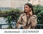 Busy businesswoman adjusts wireless earphones while walking in the city, stylishly dressed for a modern urban lifestyle