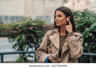 Busy businesswoman adjusts wireless earphones while walking in the city, stylishly dressed for a modern urban lifestyle