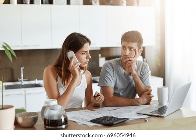 Busy Businesswoman Preparing Financial Report While Being At Home, Calling Her Business Partner Over Mobile Phone, Sitting Next To Her Husband Who Is Looking Attentively At Her, Trying To Understand