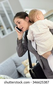 Busy businesswoman talking on phone and holding baby in arms