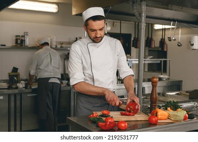 Busy Chef Cutting Red Pepper And Cucumbers On A Board For Making Salad In Modern Restaurant Kitchen