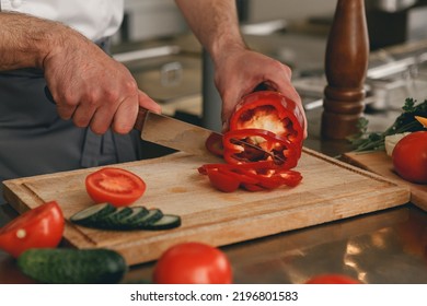 Busy Chef Cutting Red Pepper And Cucumbers On A Board For Making Salad In Modern Restaurant Kitchen