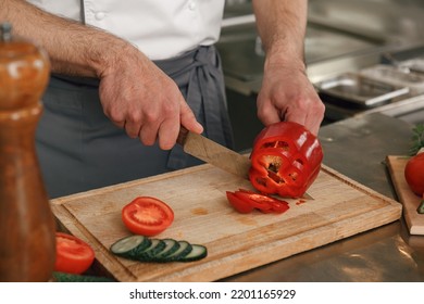 Busy Chef Cutting Red Pepper And Cucumbers On A Board For Making Salad In Modern Restaurant Kitchen