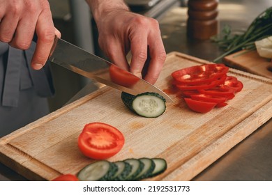 Busy Chef Cutting Tomatoes And Cucumbers On A Board In Modern Restaurant Kitchen