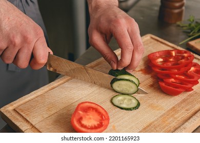 Busy Chef Cutting Tomatoes And Cucumbers On A Board In Modern Restaurant Kitchen