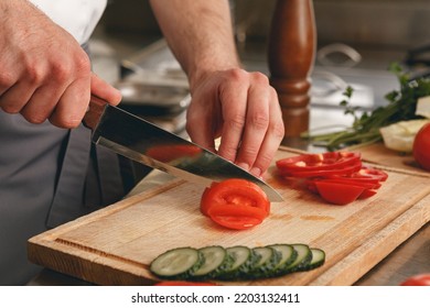 Busy Chef Cutting Tomatoes And Cucumbers On A Board In Modern Restaurant Kitchen