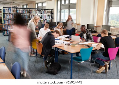 Busy College Library With Teacher Helping Students At Table