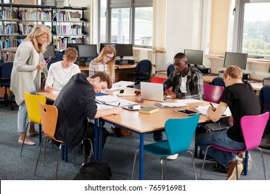 Busy College Library With Teacher Helping Students At Table