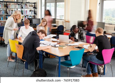 Busy College Library With Teacher Helping Students At Table