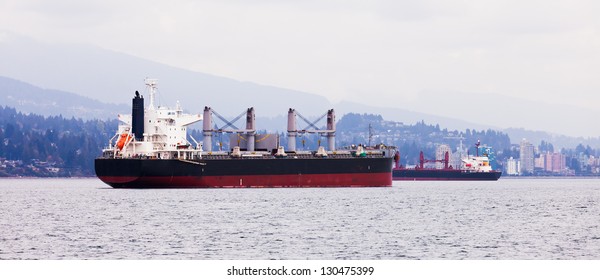 Busy commercial coastal shipping lane with two overseas freighters passing each other close to North Vancouver coastline with urban buildings