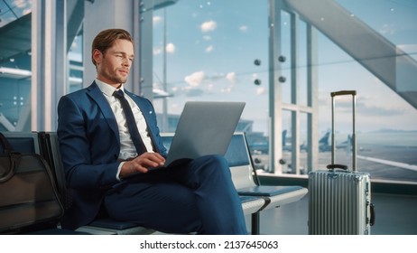 Busy Crowded Airport Terminal: Businessman Uses Laptop, Waiting For A Flight. Traveling Entrepreneur Working Online On Computer Sitting In A Boarding Lounge Of Airline Hub With Airplanes