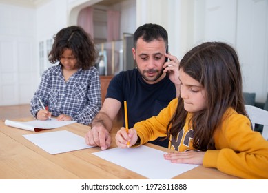 Busy Dad Drawing With Kids While Talking On Phone. Focused Girl With Dad Sitting At Table. Curly-haired Boy Standing. Family Time, Fatherhood Concept