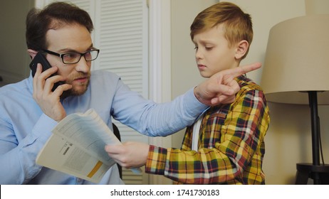 Busy Dad In Glasses Sitting At The Laptop Computer At The Desk And Talking On The Phone When His Little Son Coming And Asking To Help With Homework. Father Sending Him Out. At Home. Indoor