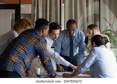 Busy diverse business team working on project together, talking, planning tasks. Employees meeting at conference table, talking, sticking notes, discussing documents. Teamwork, scrum management