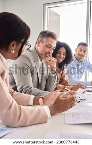 Busy diverse professional business team having discussion at office meeting. Financial advisors or managers consulting senior business man investor talking sitting at conference table. Vertical shot.