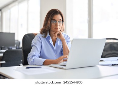 Busy elegant middle aged business woman using laptop working in corporate office. Mature professional businesswoman executive at work, female manager looking at computer at desk thinking on project. - Powered by Shutterstock