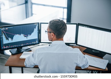 Busy employee. View from the back. Young businessman in formal clothes is in office with multiple screens. Conception of exchange and money.