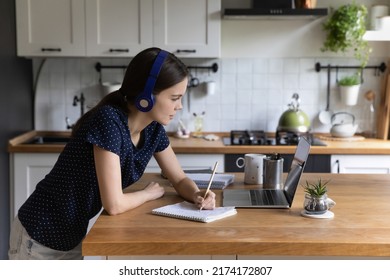 Busy Engaged College Student Girl In Wireless Headphones Using Laptop For Online Studying, Writing Essay, Notes, Preparing For Test, Watching Webinar, Lesson, Listening To Workshop, Lecture