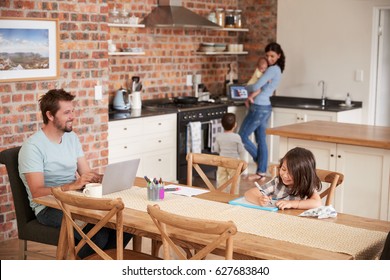 Busy Family Home With Father Working As Mother Prepares Meal