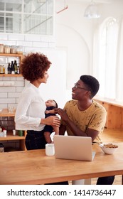 Busy Family In Kitchen At Breakfast With Father Caring For Baby Son