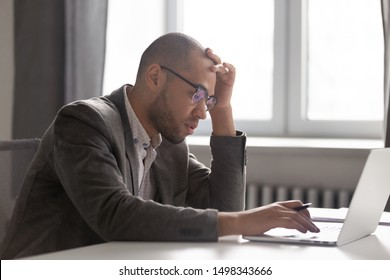 Busy fatigued african american employee solving hard problem with client online, stuck with difficult task or calculations. Overloaded tired businessman making financial company report on computer.