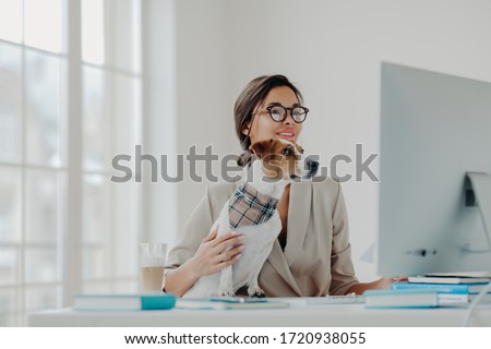 Busy female teacher wears formal clothes and spectacles conducts online lessons for students works at computer poses in coworking space with dog, busy working online. Businesswoman at desktop
