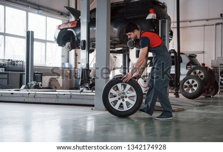 Busy guy. Mechanic holding a tire at the repair garage. Replacement of winter and summer tires.