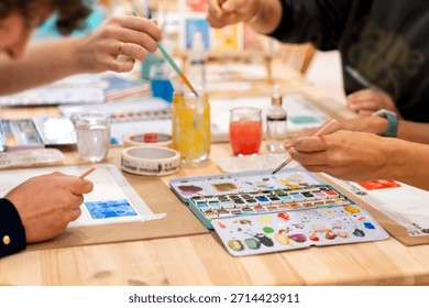 Busy hands creating artwork using watercolor paint, brushes, and palette during a hands-on art class
