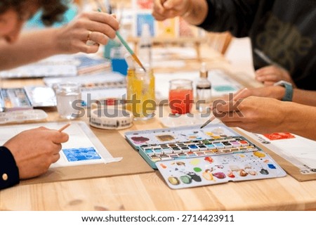 Busy hands creating artwork using watercolor paint, brushes, and palette during a hands-on art class