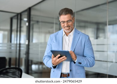 Busy happy mature older business man executive standing in office using digital tablet. Middle aged businessman corporate manager wearing suit working on tab on professional financial project. - Powered by Shutterstock