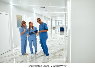 In a busy hospital corridor, a team of three healthcare professionals examines Xray images, highlighting the importance of teamwork and professionalism for patient safety in healthcare - Powered by Shutterstock