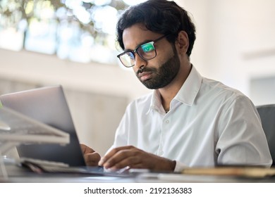 Busy Indian Business Man Office Employee Worker, Arab Professional Company Manager Analyst Wearing Eyeglasses Working On Corporate Data Typing On Laptop Computer Sitting At Home Office Work Desk.