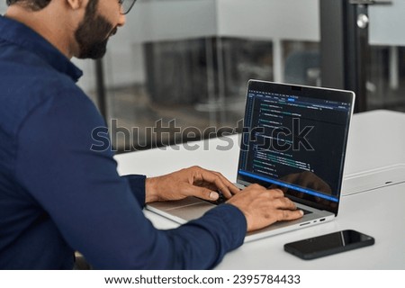 Busy Indian business man software developer engineer working on laptop computer in office. Male administrator programmer specialist coding on pc developing applications. Over shoulder screen view.