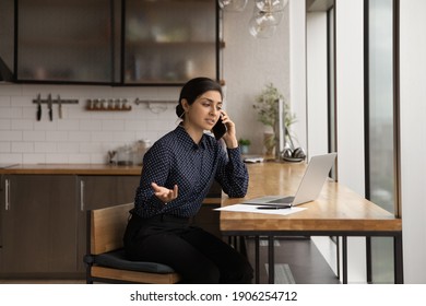 Busy Indian Female Consultant Give Recommendation To Client By Cell Reading Documents Opened On Laptop Screen. Doubtful Hindu Lady Engaged In Remote Work Ask Colleague For Advice At Phone Conversation