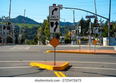 A busy intersection features active railroad crossing gates, traffic lights, and multiple directional signs indicating lane usage and turns