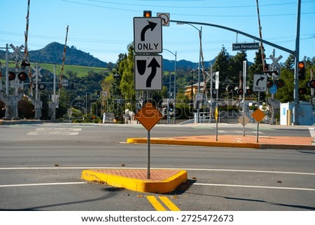 A busy intersection features active railroad crossing gates, traffic lights, and multiple directional signs indicating lane usage and turns