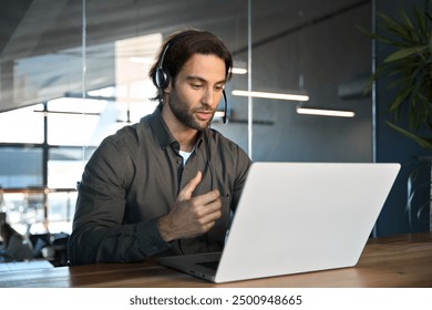 Busy male support service operator talking to customer sitting at desk. Young professional business man call contact center agent wearing headset working in business office using laptop computer.