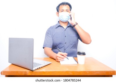 A Busy Man Wearing Mask Obeying Covid-19 SOP, Talking On The Phone With His Client During Working Hours In The Office.