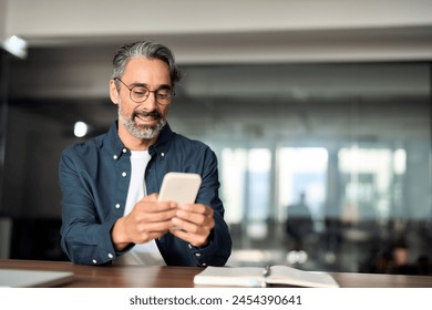 Busy mature business man entrepreneur investor sitting at desk using mobile cell phone. Middle aged businessman executive looking at cellphone device working investing finances holding smartphone. - Powered by Shutterstock