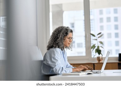 Busy mature senior business woman working in office using laptop. Middle aged old professional lady executive manager looking at computer digital technology sitting at desk. Authentic candid shot. - Powered by Shutterstock