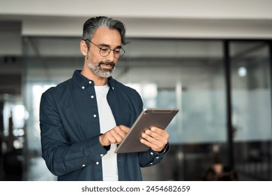 Busy middle aged business man wearing shirt standing in corporate office using digital tablet. Mature older businessman professional executive manager investor working on fintech tab computer device. - Powered by Shutterstock