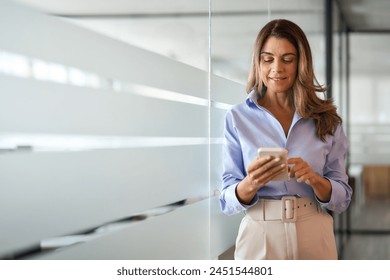 Busy middle aged businesswoman executive using mobile phone standing in office. Smiling mature business woman entrepreneur looking at smartphone holding cellphone managing finances banking data. - Powered by Shutterstock