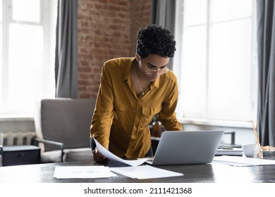 Busy millennial African entrepreneur woman reviewing online reports, using laptop computer. Freelance employee, businesswoman working in home office, doing paperwork job, standing at table - Shutterstock ID 2111421368