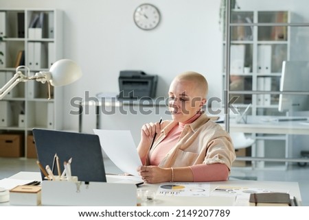 Busy modern Caucasian businesswoman with bald hairstyle sitting at office desk and working with papers