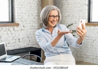 Busy Modern Mature Businesswoman In Glasses And Casual Attire, Standing In The Office, Taking Break To Video Call And Talk With Her Family, Looking At Mobile Phone And Asking How Are You Question