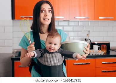 Busy Mom Cooking  Holding Baby In Carrier Baby Wearing System. Mom Making Cookies Carrying Newborn Around The Kitchen
