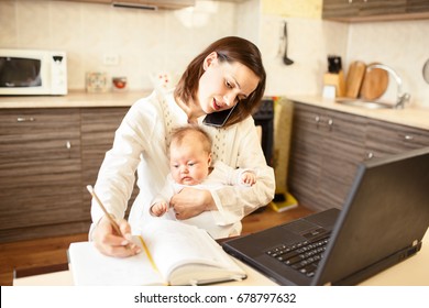 Busy Mom Writing In Notepad While Holding A Baby