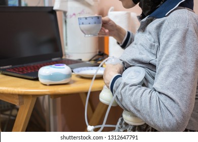 Busy Mother Pumping Breastmilk With Automatic Breast Pump Machine While Drinking Coffee.